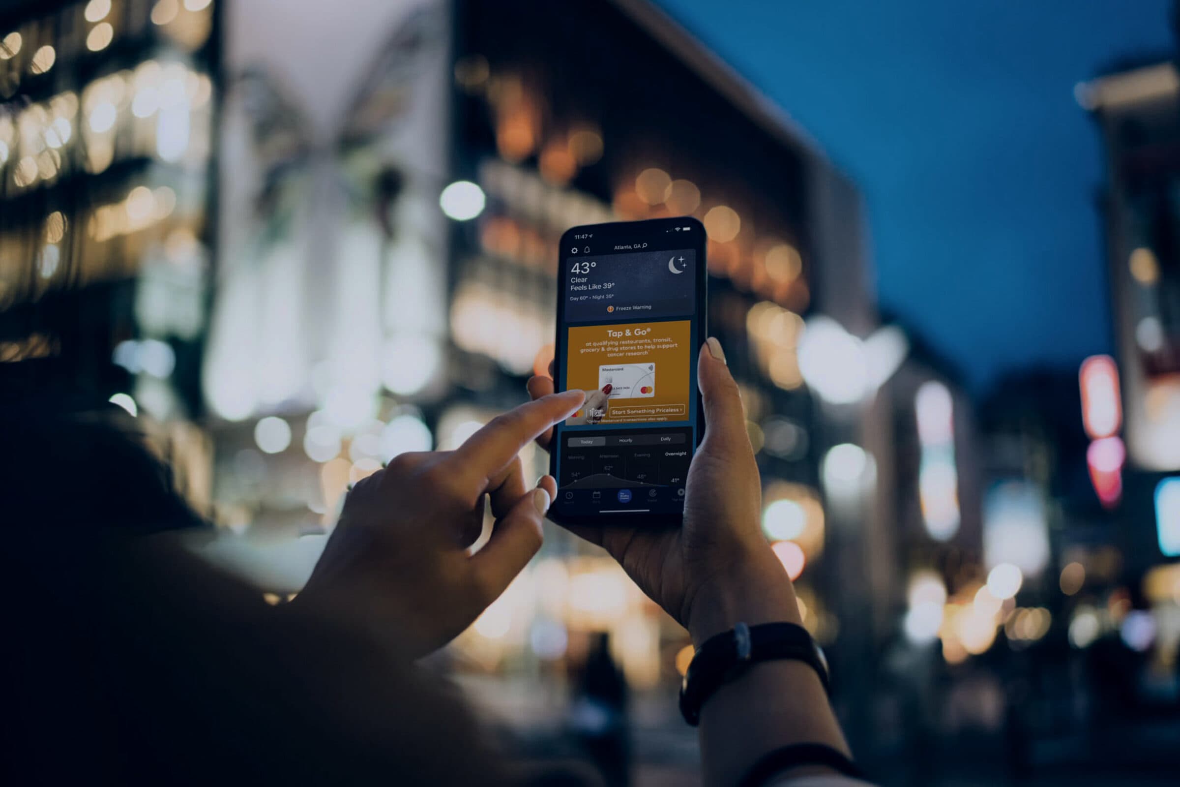 A hand holding a phone on a neon-lit street at night