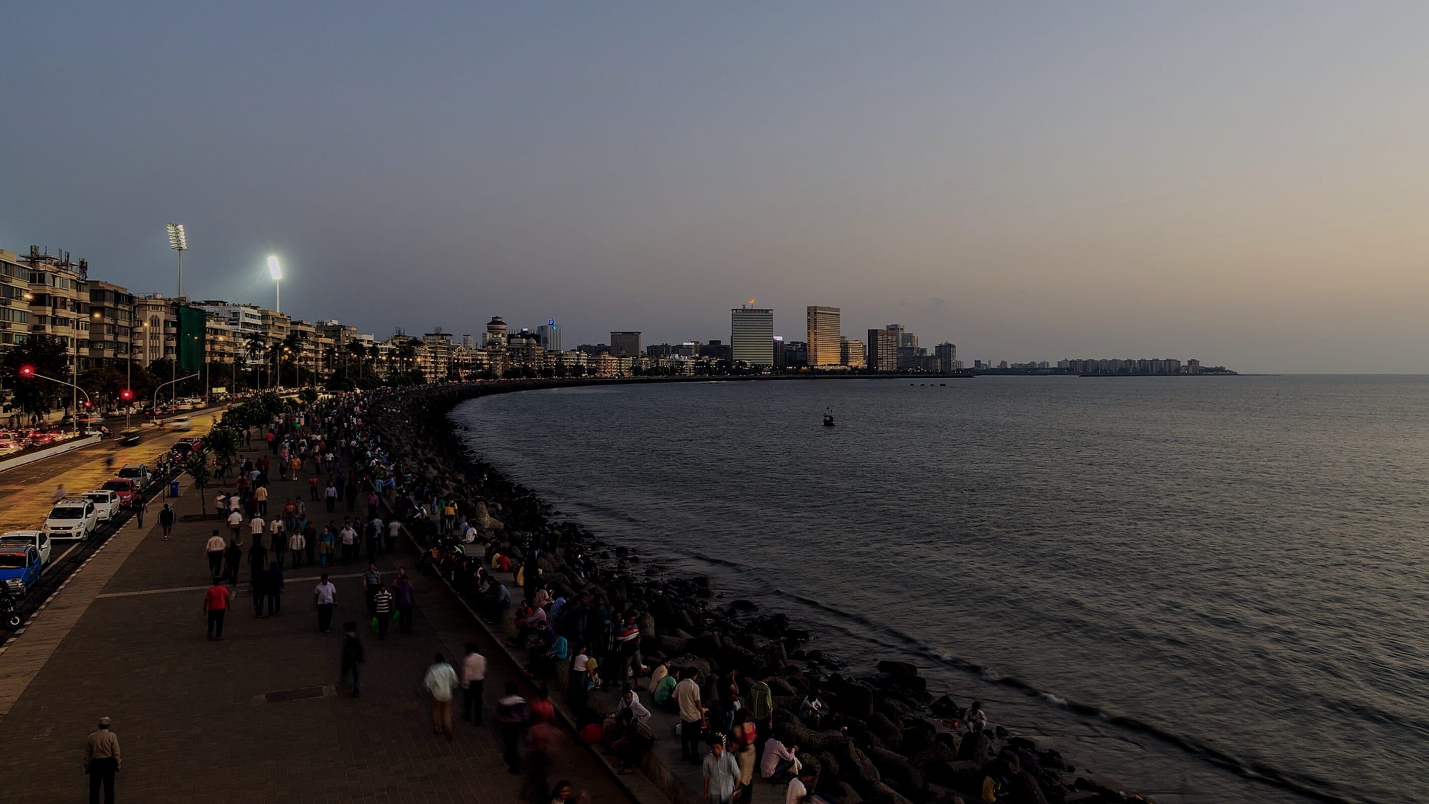 A crowd gathered along the seafront at dusk